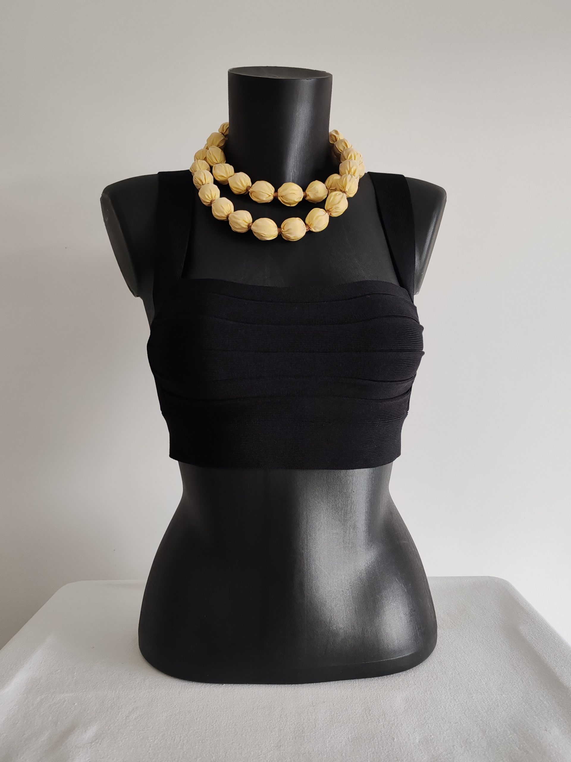 Sautoir modulable réalisé en perles de taffetas de soie jaune clair - 2 cm. Se porte en long, en double tour de cou, ou en ceinture. Présenté sur buste noir de face.