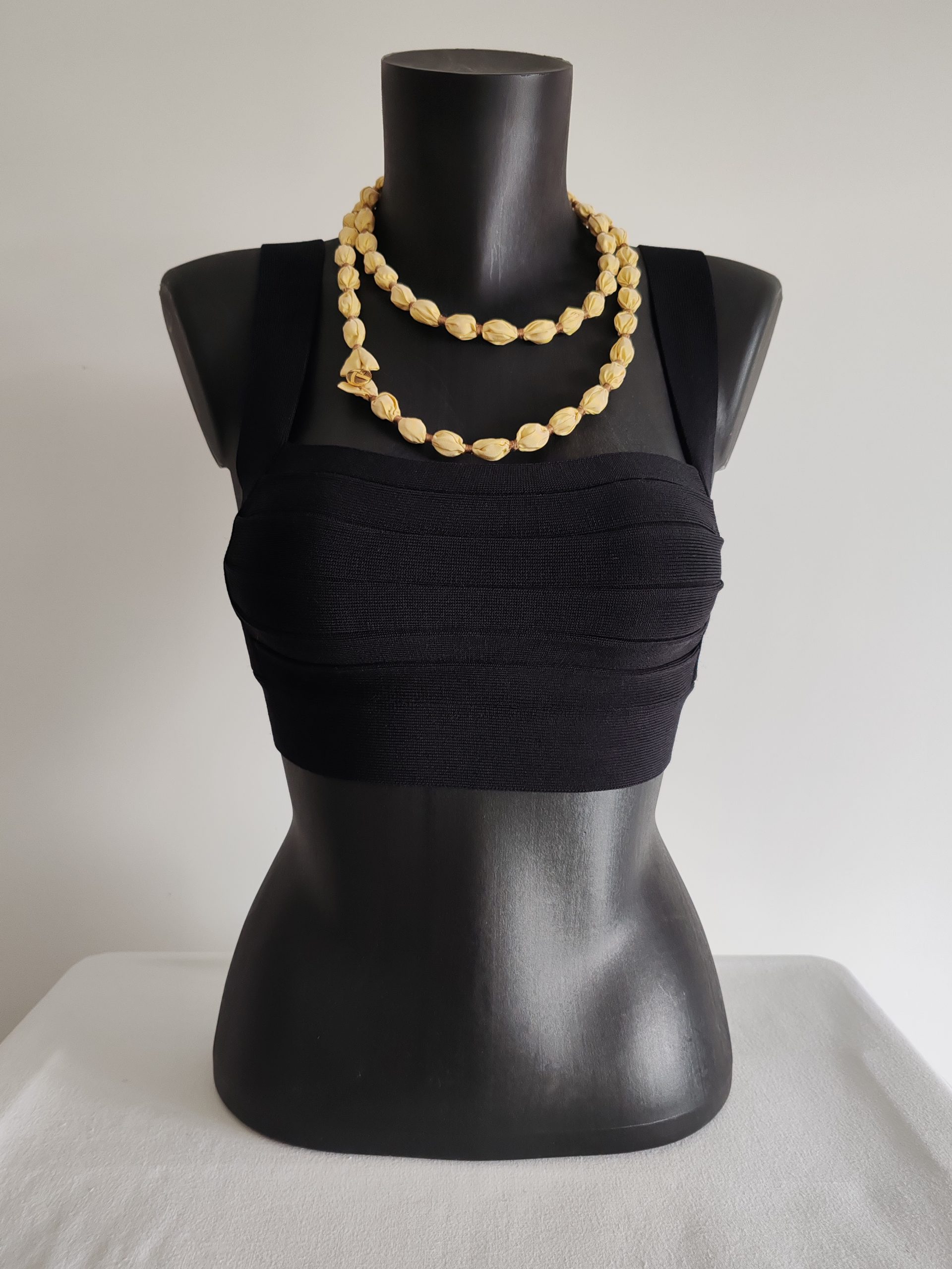 Collier sautoir modulable réalisé en perles de taffetas de soie jaune clair. Se porte en long, en double tour de cou, ou en ceinture. Présenté sur buste noir de face.