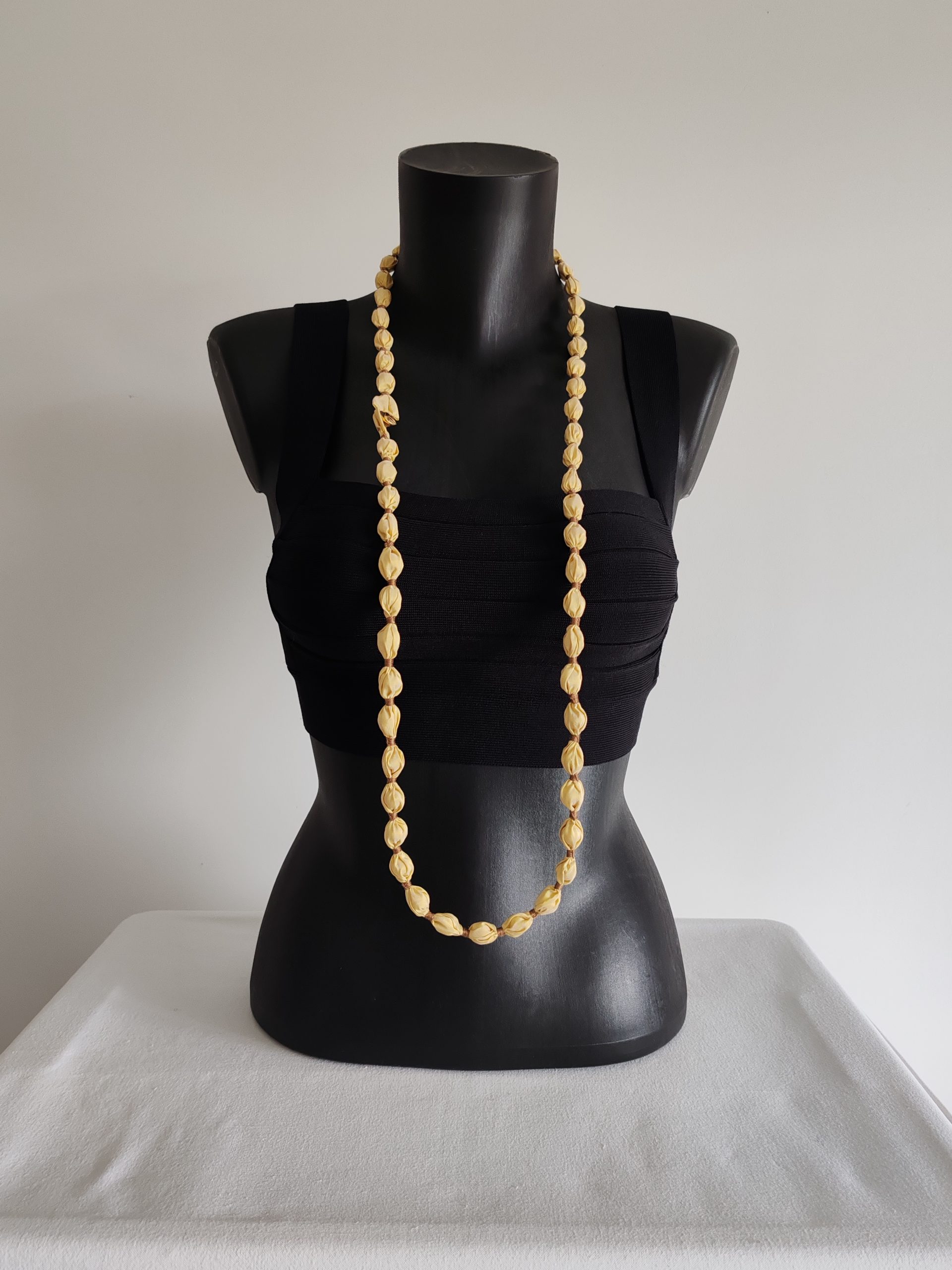 Collier sautoir Naïla en taffetas de soie jaune clair et fil de coton doré, présenté simple sur un buste noir