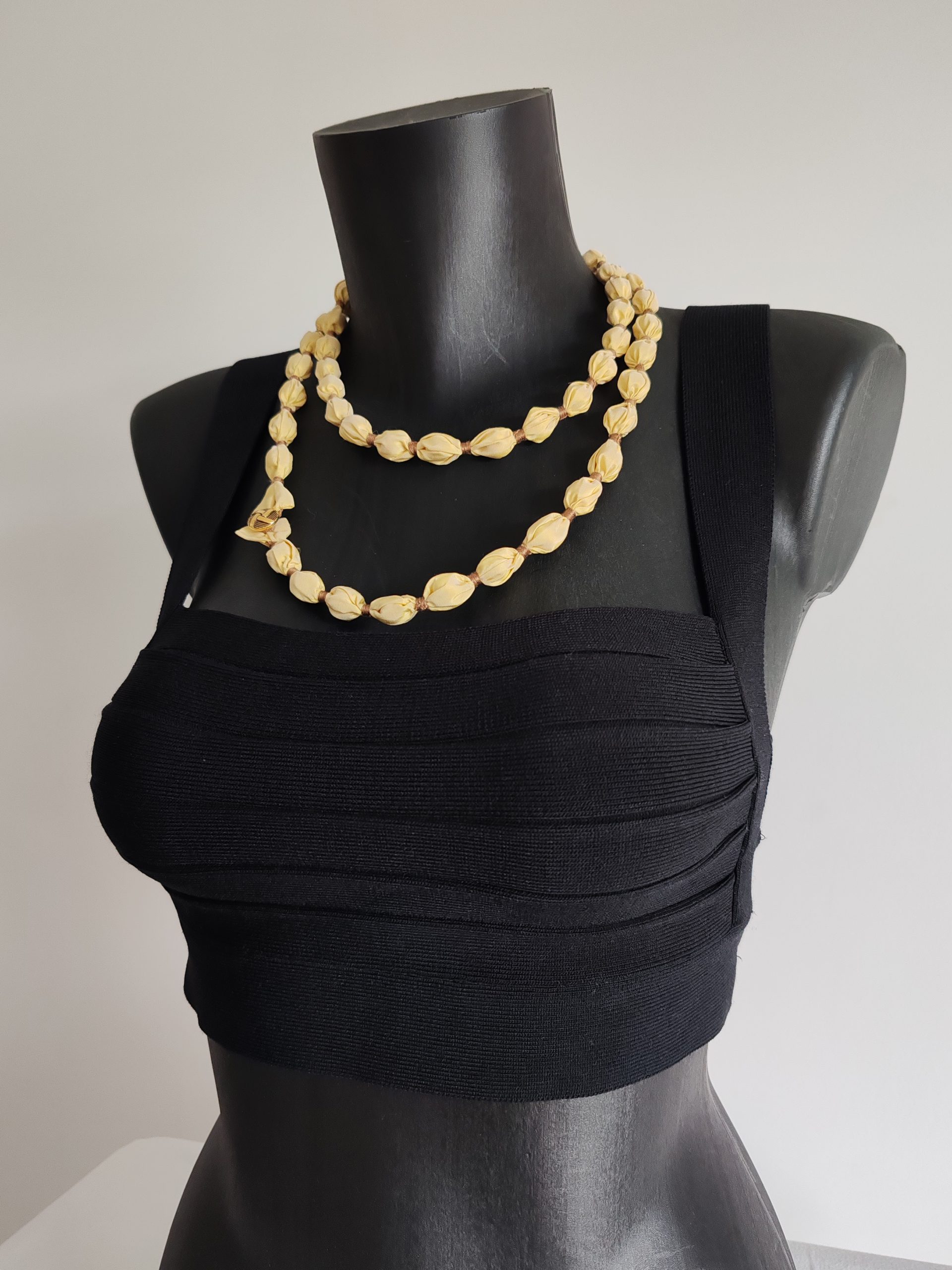 Gros plan du collier sautoir Naïla en taffetas de soie jaune clair et fil de coton doré, présenté double rang sur un buste noir