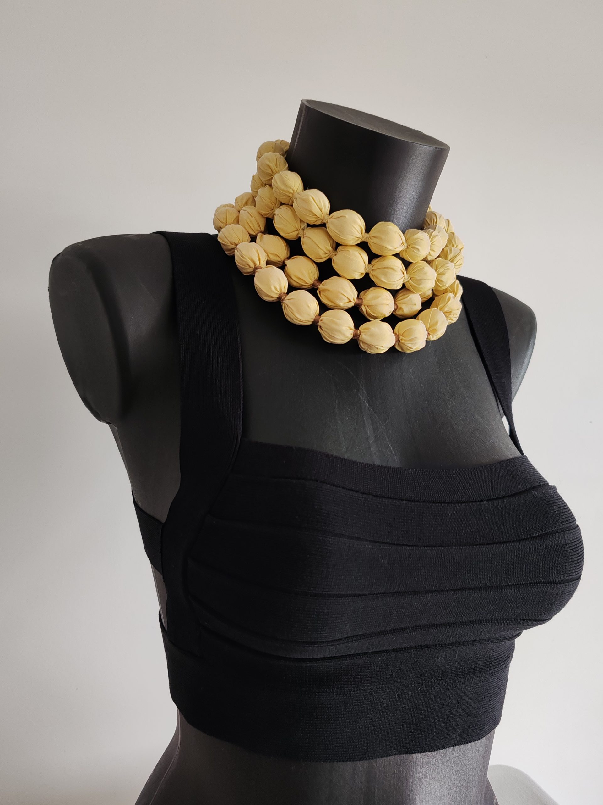 Gros plan du sautoir modulable réalisé en perles de taffetas de soie jaune clair - 2 cm. présenté en multiple rangs autour du cou, sur buste noir de face.