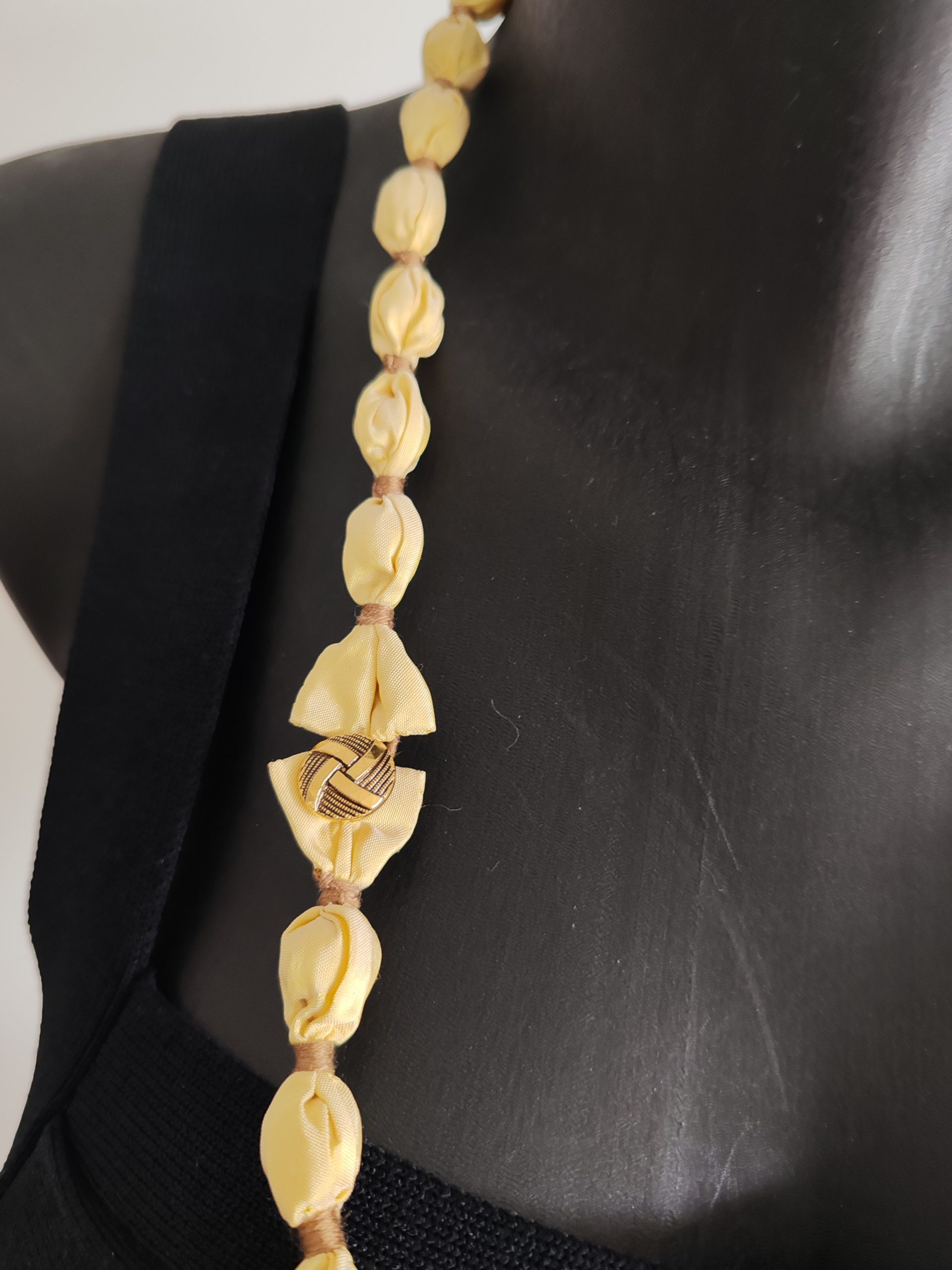 Zoom sur le fermoir du sautoir Naïla en taffetas de soie jaune clair et fil de coton doré, présenté double rang sur un buste noir